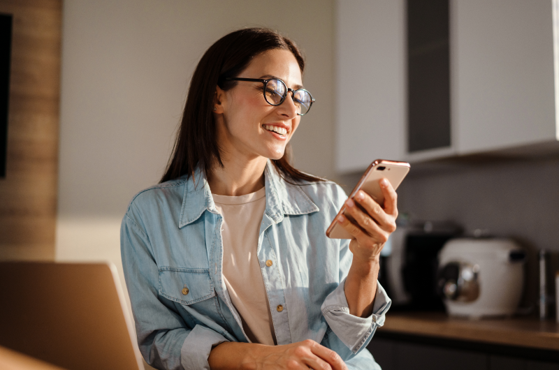 O que é o Tenda Play? | Foto de uma mulher sorrindo enquanto usa o celular | Trilha da Conquista | Blog da Tenda