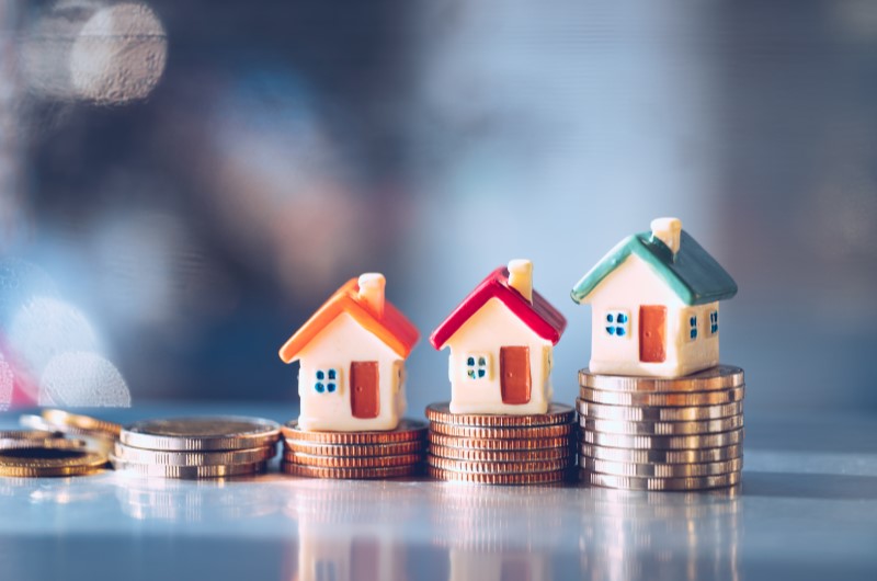 Taxa de juros reduzidas | Foto de três casinhas em cima de algumas moedas | Minha Casa, Minha Vida | Blog da Tenda