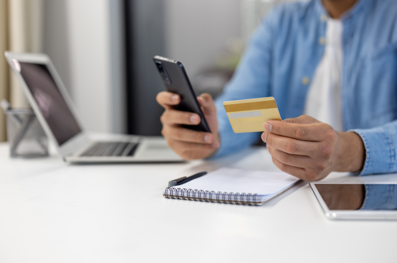 Evite fazer novas dívidas | Foto de um homem segurando um cartão de crédito e um celular | Como limpar o seu nome | Eu Dou Conta 