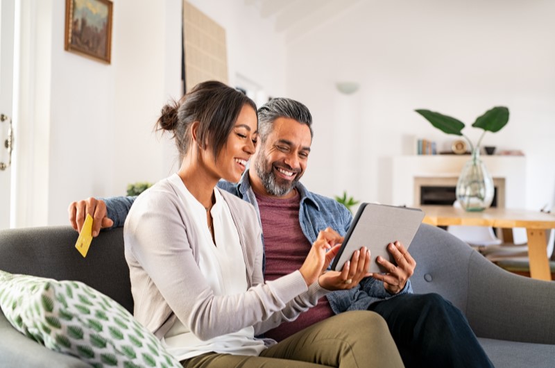 Infraestrutura | Foto de um casal sorridente sentado no sofá enquanto olha para um tablet | Trilha da Conquista | Blog da Tenda 