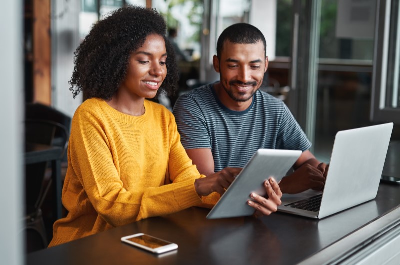 O que é o Minha Casa, Minha Vida 2024? | Foto de um casal sorridente usando um tablet e um notebook | Minha Casa Minha Vida | Blog da Tenda