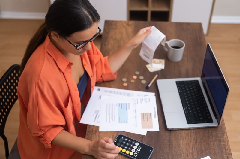 O que são despesas de casa? | Foto de uma mulher organizando as contas e usando a calculadora | Economia e renda extra | Eu Dou Conta 