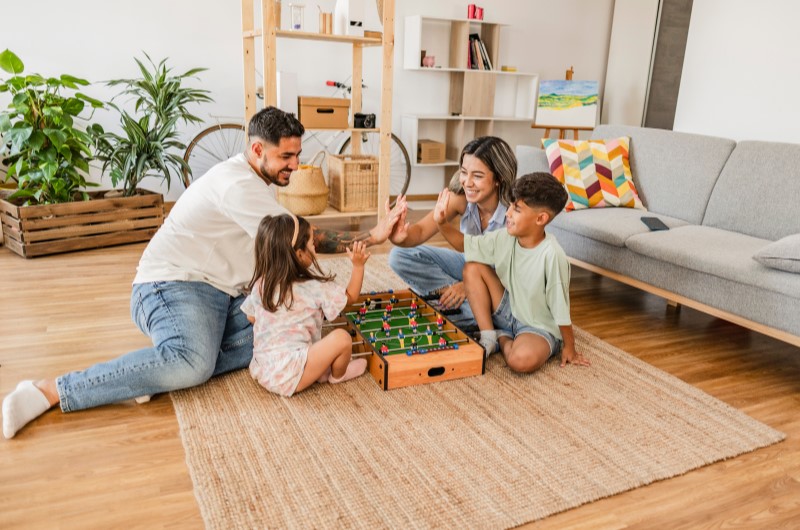 Ideias divertidas | Foto de uma família reunida na sala enquanto joga um jogo de tabuleiro | Economia e renda extra | Eu Dou Conta 