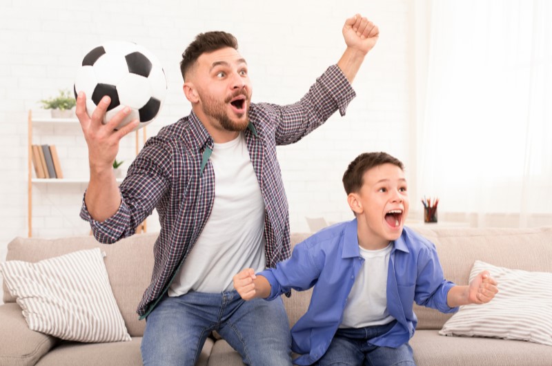 Presente para o Dia dos Pais: fã de esporte | Foto de um pai e filho animados enquanto assistem uma partida de futebol | Economia e renda extra | Eu Dou Conta