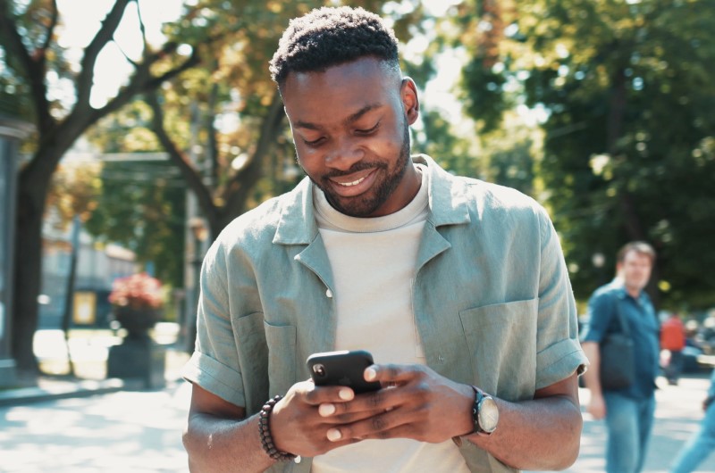 Conheça a vizinhança | Homem sorridente usando o celular ao ar livre | Casa e decoração | Blog da Tenda 