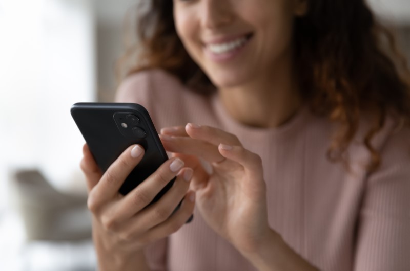 Comércios e serviços | Foto de uma mulher sorrindo enquanto usa o celular | Trilha da Conquista | Blog da Tenda 