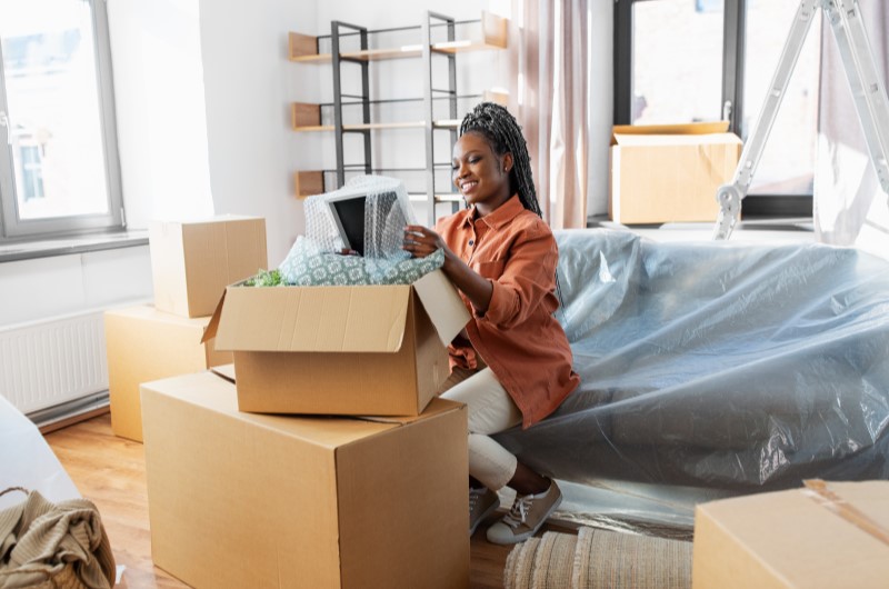 Quanto custa morar sozinho? | Foto de uma mulher sorrindo enquanto organiza sua mudança para uma casa nova | Economia e renda extra | Eu Dou Conta