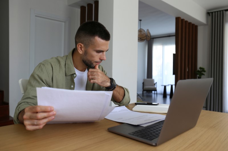 Renda mensal | Homem segurando alguns documentos e usando o notebook | Dúvidas sobre dívidas | Eu Dou Conta 