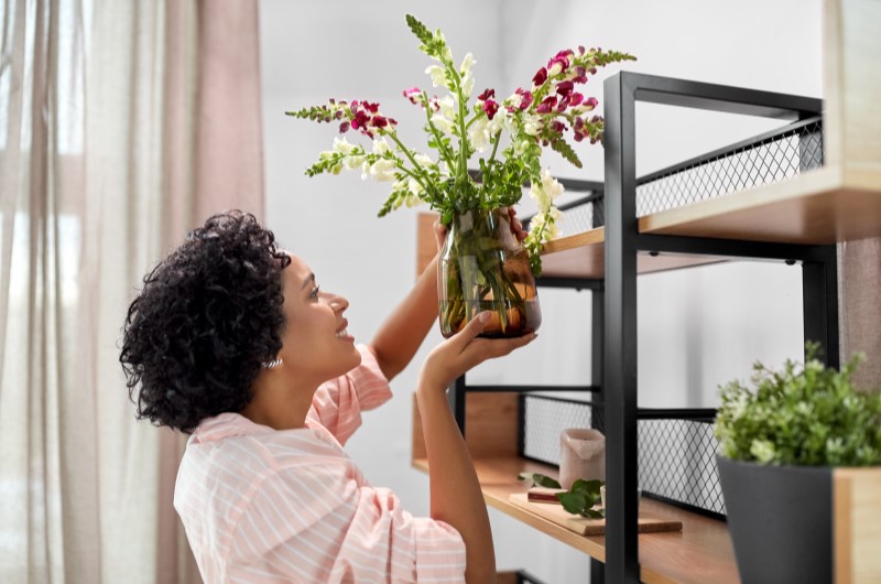 7 dicas de decoração de primavera | Mulher colocando um vaso de flores em uma estante | Casa e Decoração | Blog da Tenda 