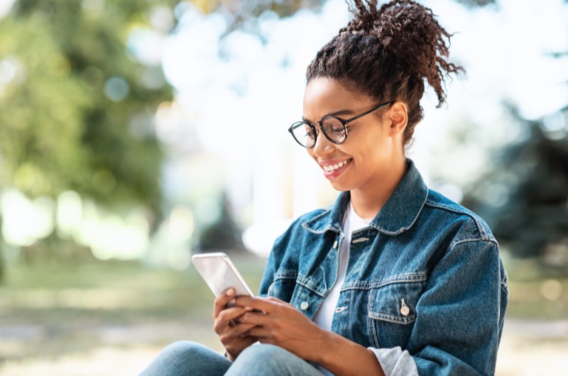 Conheça a cultura da região | Mulher sorrindo enquanto usa o celular | Trilha da Conquista | Blog da Tenda