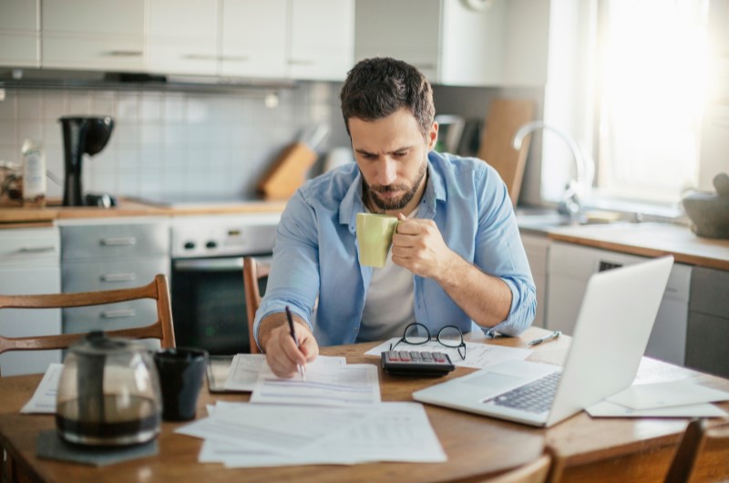 Entenda sua situação financeira antes de começar | Homem pensativo organizando as finanças | Trilha da Conquista | Blog da Tenda 