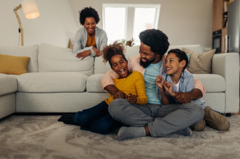 Santa Cruz | Família sorridente se divertindo na sala de estar de casa | Trilha da Conquista | Blog da Tenda