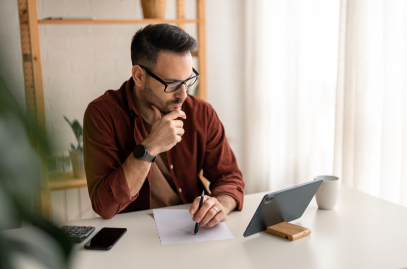 Aguarde a análise de crédito | Homem pensando enquanto toma notas em frente ao tablet | Minha Casa Minha Vida | Blog da Tenda