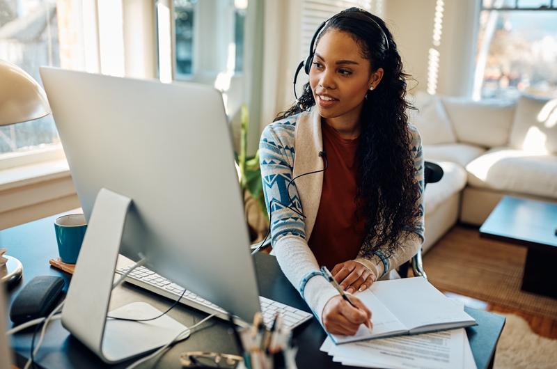 Mantenha o espaço organizado no seu home office | Mulher anotando em um caderno enquanto usa o computador | Casa e Decoração | Blog da Tenda 