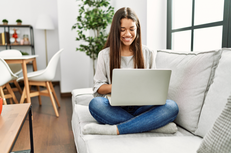 O que é a área comum do condomínio | Mulher sorridente usando o notebook no sofá da sala | Viver em Condomínio | Blog da Tenda 