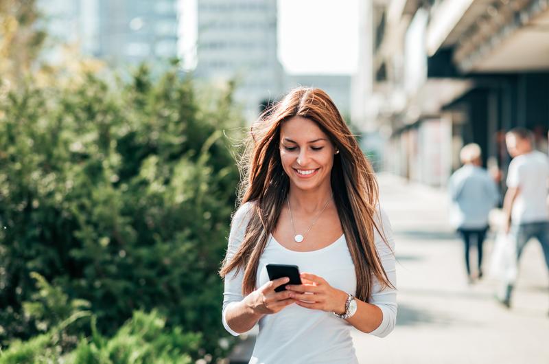 Onde fica a Zona Norte de Recife | Mulher sorridente enquanto caminha e usa o celular | Trilha da Conquista | Blog da Tenda 