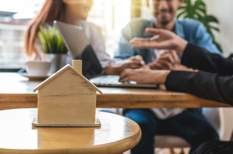 O que é averbação de imóvel | Três pessoas conversando ao fundo com uma casinha em miniatura na frente | Tenda Explica | Blog da Tenda 