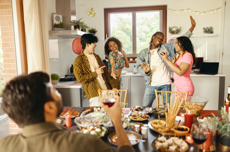 O que observar nas festas de final de ano em condomínio | Amigos dançando e comemorando em uma festa animada ao redor de uma mesa de comida | Viver em Condomínio | Blog da Tenda 