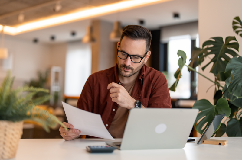 Como emitir a matrícula do imóvel | Homem revisando documentos em casa, com notebook e calculadora na mesa | Tenda Explica | Blog da Tenda 