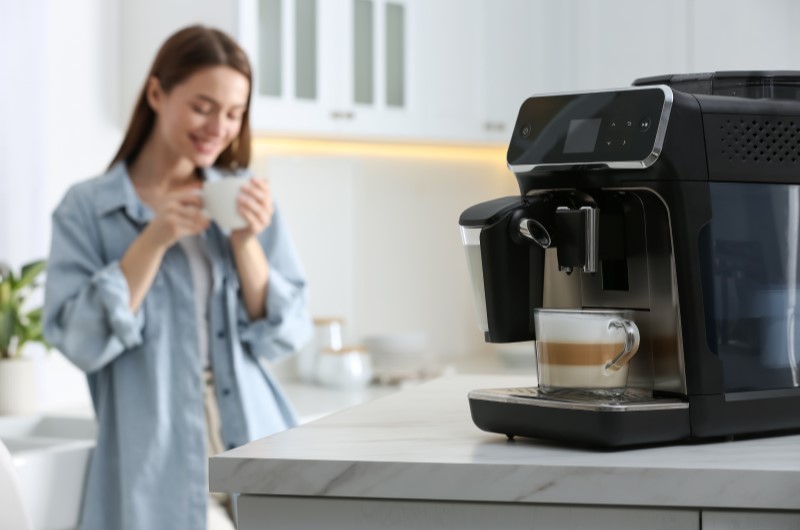 Como fazer um cantinho do café simples e barato | Máquina de café expresso em uso, com mulher sorrindo ao fundo | Casa e Decoração | Blog da Tenda 