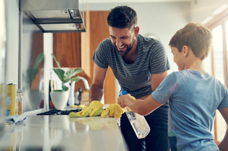 Dicas para limpeza de casa | Mulher usando luvas e limpando a superfície branca com pano verde e produto de limpeza | Casa e Decoração | Blog da Tenda 