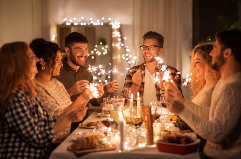 Iluminação festiva | Grupo de amigos sorrindo e segurando luzes durante uma celebração festiva à mesa | Casa e Decoração | Blog da Tenda