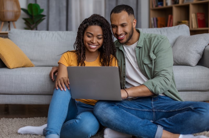 O que é um apartamento funcional | Casal sentado no chão usando notebook na sala de estar | Casal relaxando juntos no sofá da sala em um apartamento funcional | Casa e Decoração | Blog da Tenda 