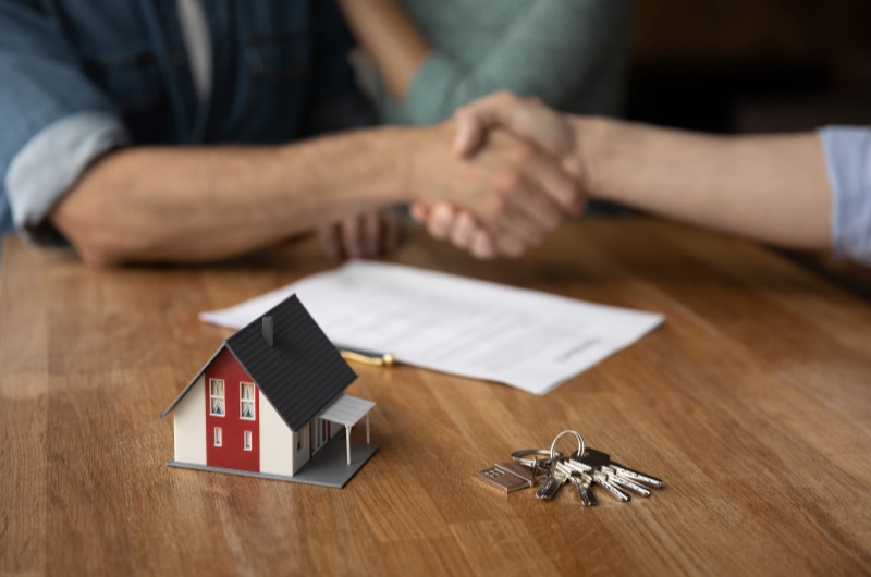 Quando é necessário fazer uma averbação no documento | Aperto de mãos sobre a mesa, com miniatura de casa e chaves em destaque | Tenda Explica | Blog da Tenda