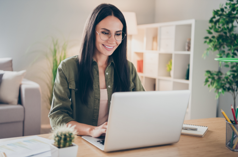 Quanto custa para emitir a matrícula do imóvel | Mulher sorrindo enquanto trabalha em um notebook em ambiente iluminado | Tenda Explica | Blog da Tenda 