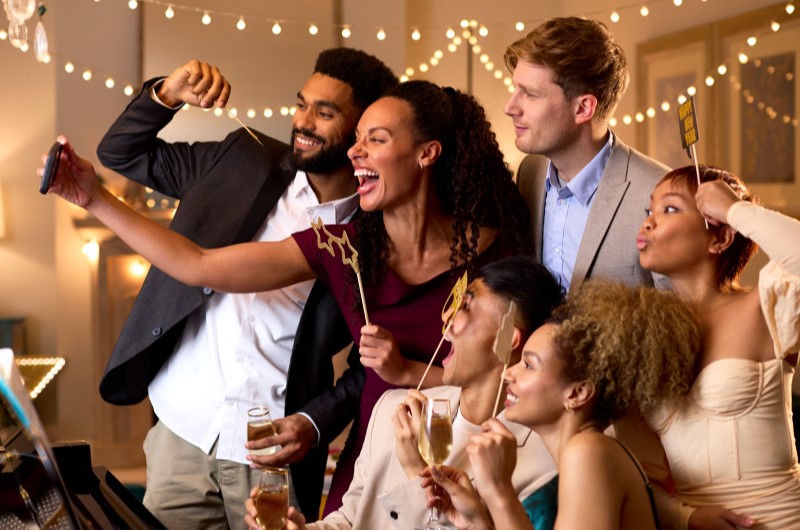 Utilize elementos coloridos | Grupo de amigos bem-vestidos tirando uma selfie juntos durante uma celebração com luzes decorativas | Casa e Decoração | Blog da Tenda