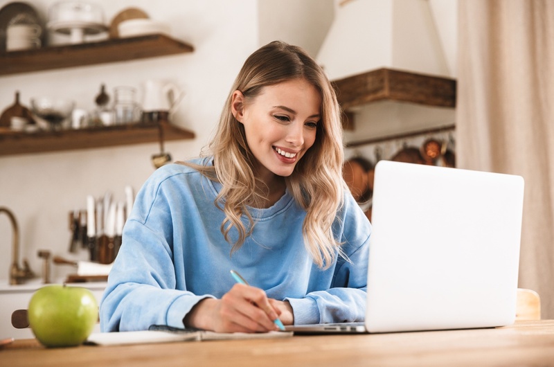 Menos manutenção | Mulher sorrindo e fazendo anotações com um notebook na mesa | Viver em Condomínio | Blog da Tenda 