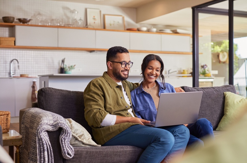 Uso das áreas comuns | Casal sentado no sofá, sorrindo e usando um notebook | Blog da Tenda 