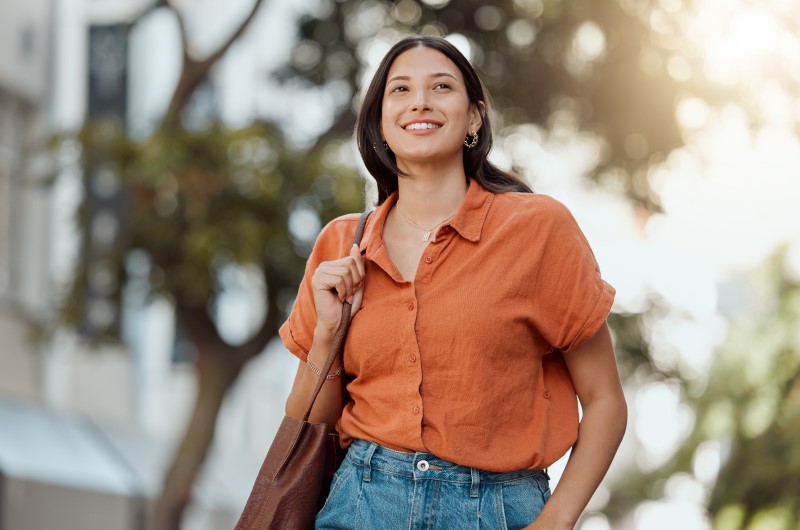 Conheça outros pontos da cidade | Mulher sorridente caminhando ao ar livre | Onde morar | Blog da Tenda 