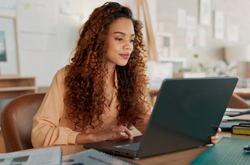 Desenvolvimento de carreira em todas as etapas | Mulher de cabelos cacheados usando notebook em um escritório | Jeito Tenda de Ser | Blog da Tenda 