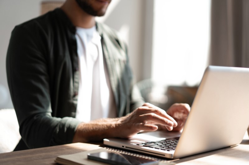 Negocie diretamente com a construtora | Homem usando notebook em uma mesa iluminada pela luz natural | Trilha da Conquista | Blog da Tenda 