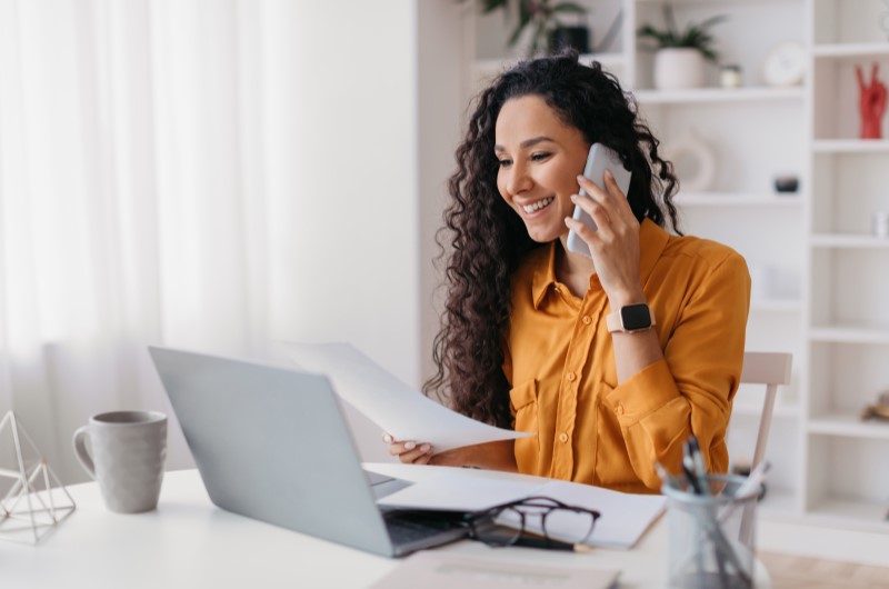 O que é a Compra Planejada | Mulher falando ao telefone enquanto segura documentos e utiliza o notebook | Eu Dou Conta | Blog da Tenda 