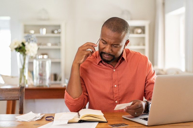 Tenha cuidado com o uso do cartão de crédito | Homem ao telefone analisando contas em casa com notebook e caderno | Eu Dou Conta | Blog da Tenda 