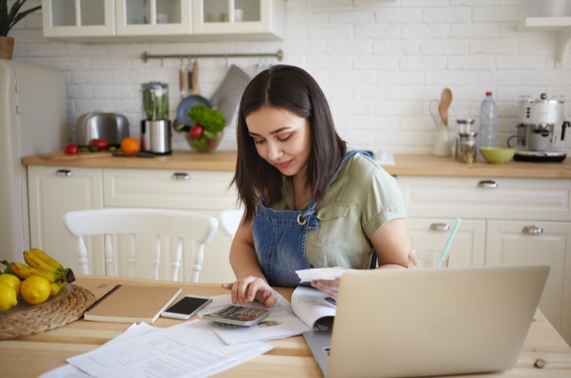 Como economizar dinheiro no dia a dia | Jovem calculando despesas com notas e planilhas na cozinha | Eu Dou Conta | Blog da Tenda 