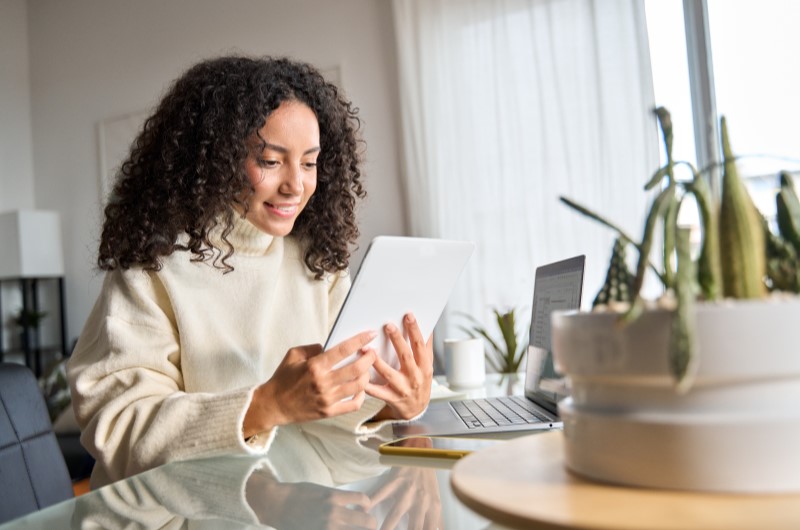 Como funciona a tabela Price | Mulher sorrindo enquanto utiliza um tablet ao lado do notebook | Trilha da Conquista | Blog da Tenda 