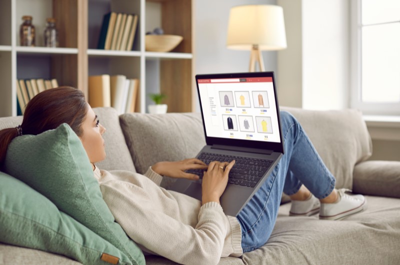 Evite compras por impulso | Mulher relaxando no sofá enquanto faz compras online no notebook | Eu Dou Conta | Blog da Tenda 