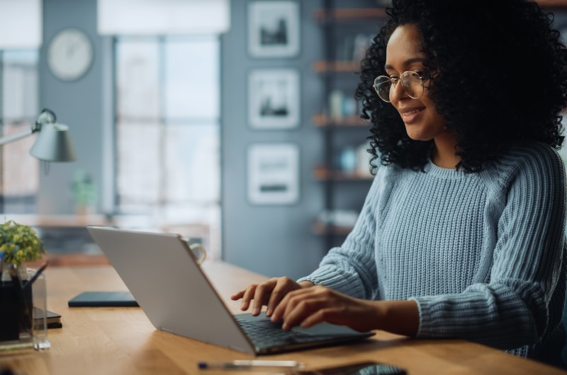 O que é o subsíndico | Mulher sorrindo enquanto trabalha no notebook | Viver em Condomínio | Blog da Tenda
