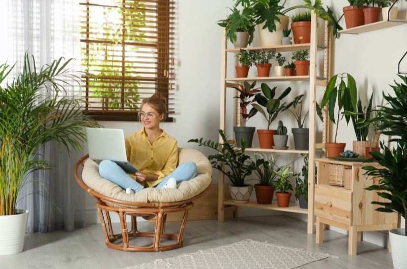 O que é um jardim vertical | Mulher sentada em uma cadeira cercada por plantas, usando um notebook | Casa e Decoração | Blog da Tenda 