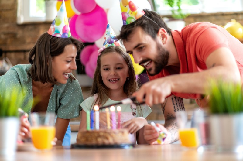 Ideias de decoração para festa de aniversário gastando pouco | Foto de uma família reunida ao redor de um bolo de aniversário | Economia e renda extra | Eu Dou Conta 