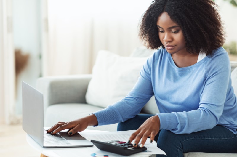 O que é o método 50, 30, 20? | Foto de uma mulher concentra em usar o notebook e uma calculadora | Economias e renda extra | Eu Dou Conta 